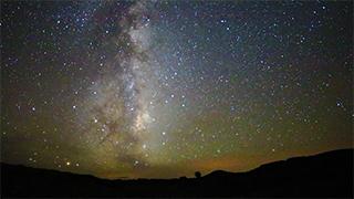 银河系的夜间图像，前景中有岩石的剪影.