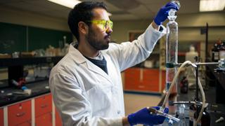 化学实验室里的一名男学生正在把一个烧杯里的液体倒进一个更大的试管里.